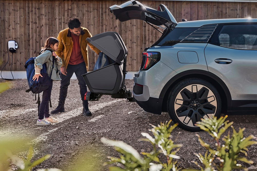 Een man en kind doen een opgevouwen kinderwagen in de open kofferbak van een Ford Explorer SUV.
