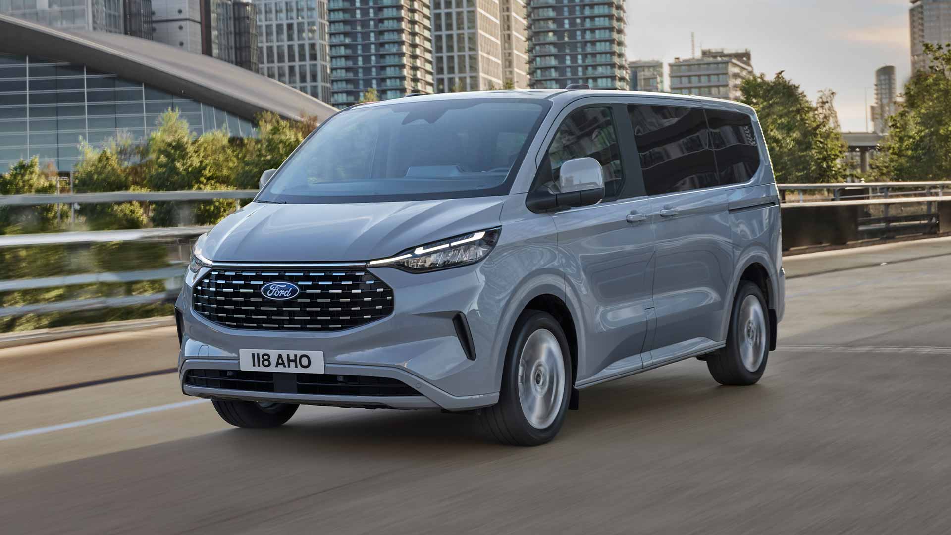 Een zilverkleurige  Ford Tourneo Custom rijdt op een stadsweg.