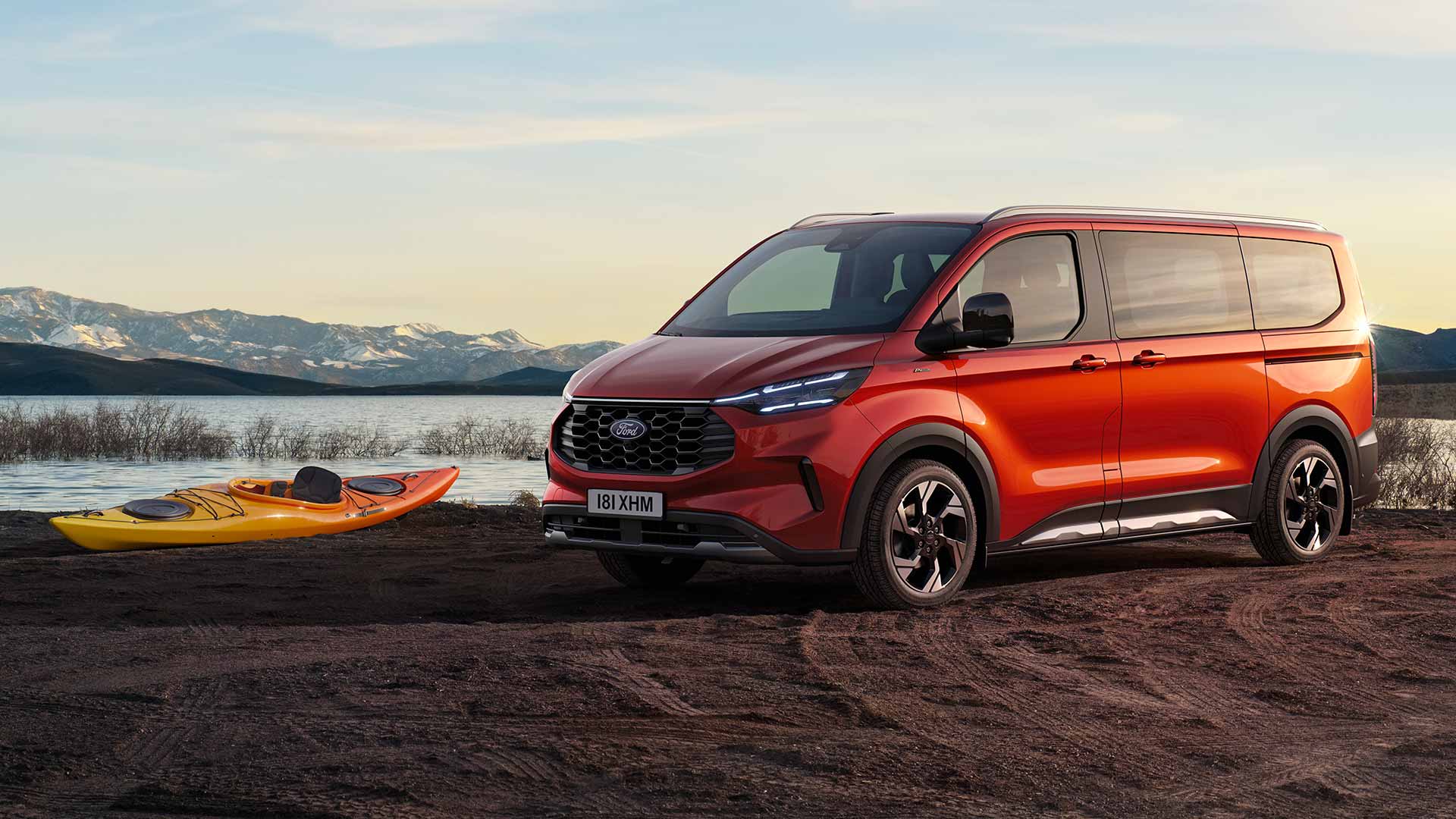 Een rode Ford Tourneo Custom bestelwagen staat geparkeerd bij een meer met een kajak. 