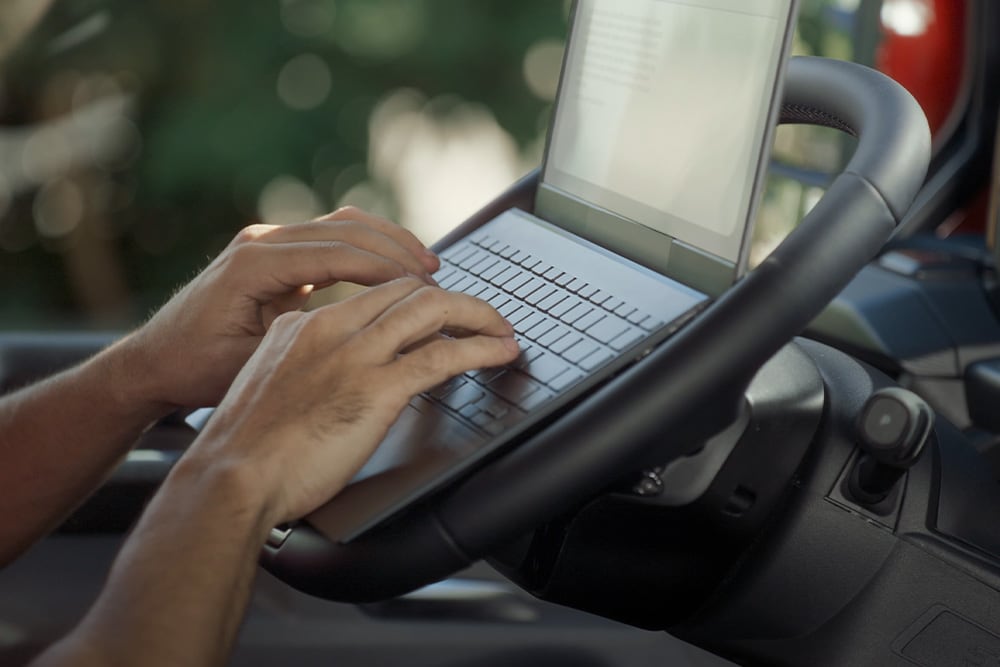 De handen van een persoon typen op een laptop die op het neerklapbare stuurwiel van de Ford Tourneo Custom is geplaatst.