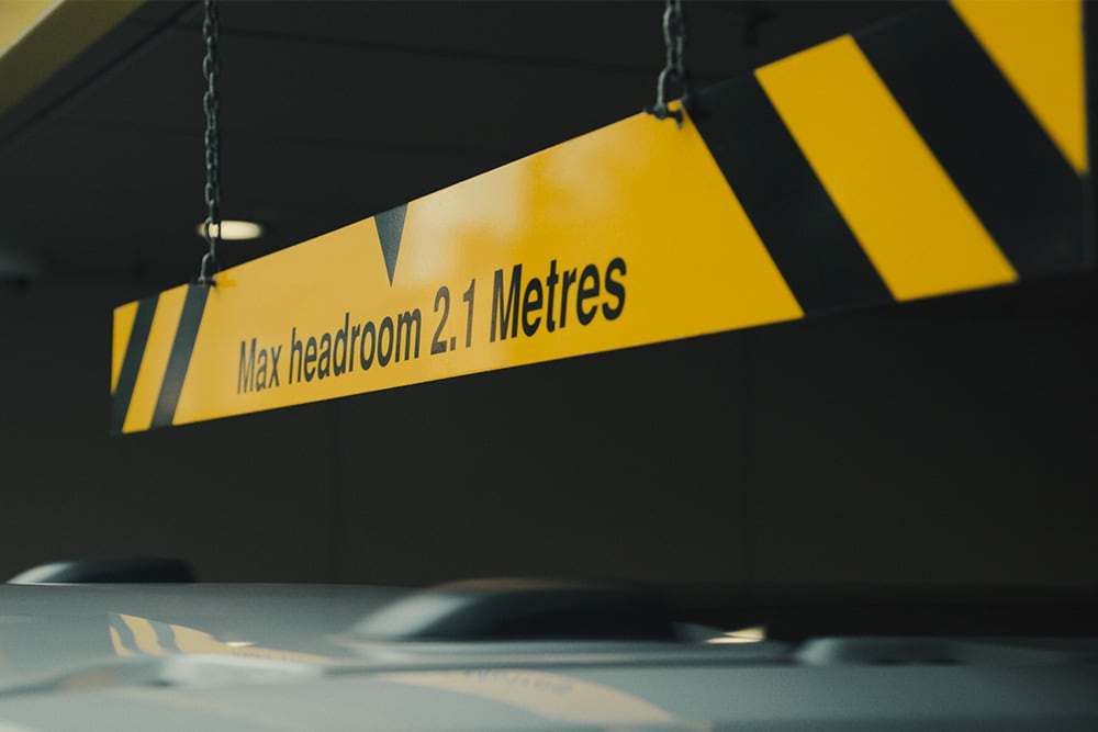 Geel en zwart bord in een parkeergarage met de tekst "Max stahoogte 2,1 meter".
