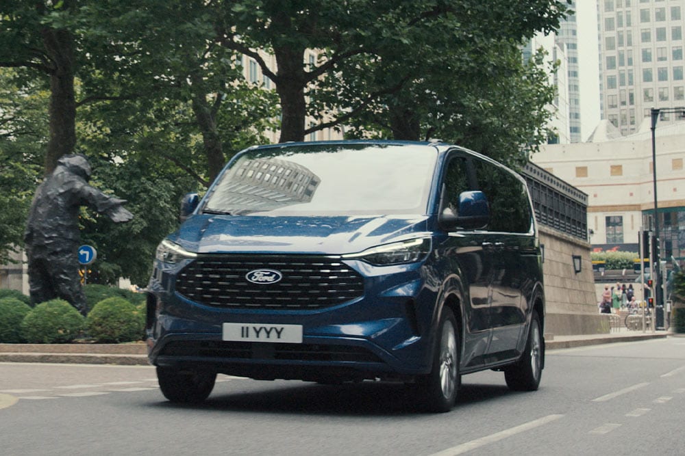 Een blauwe Ford Tourneo Custom rijdt op een stadsweg.