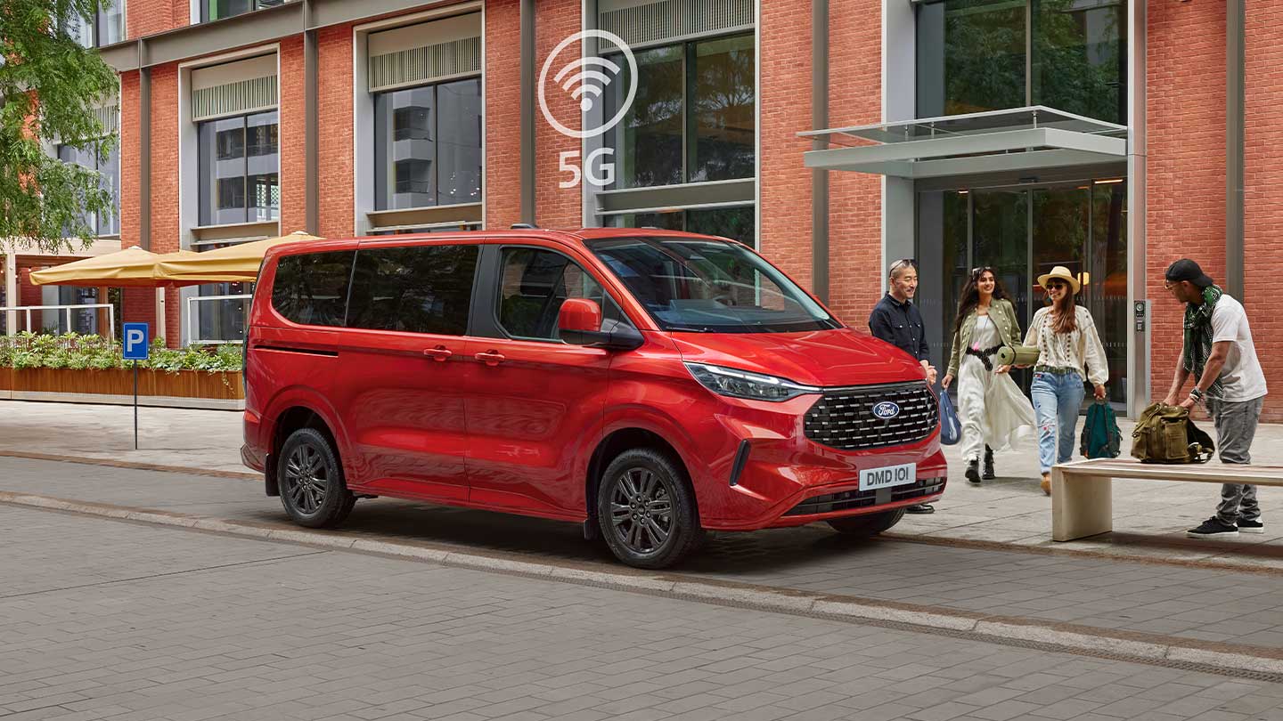 Een rode Ford Tourneo Custom staat geparkeerd in een stadsstraat voor een bakstenen gebouw