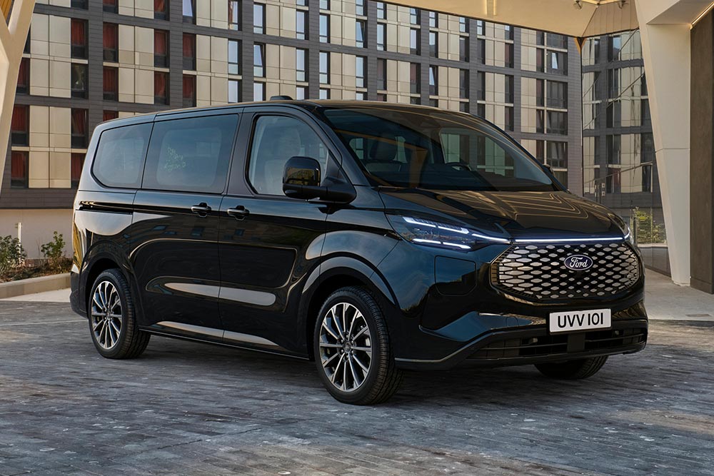 Een zwarte Ford E-Tourneo Custom staat geparkeerd voor een modern gebouw.