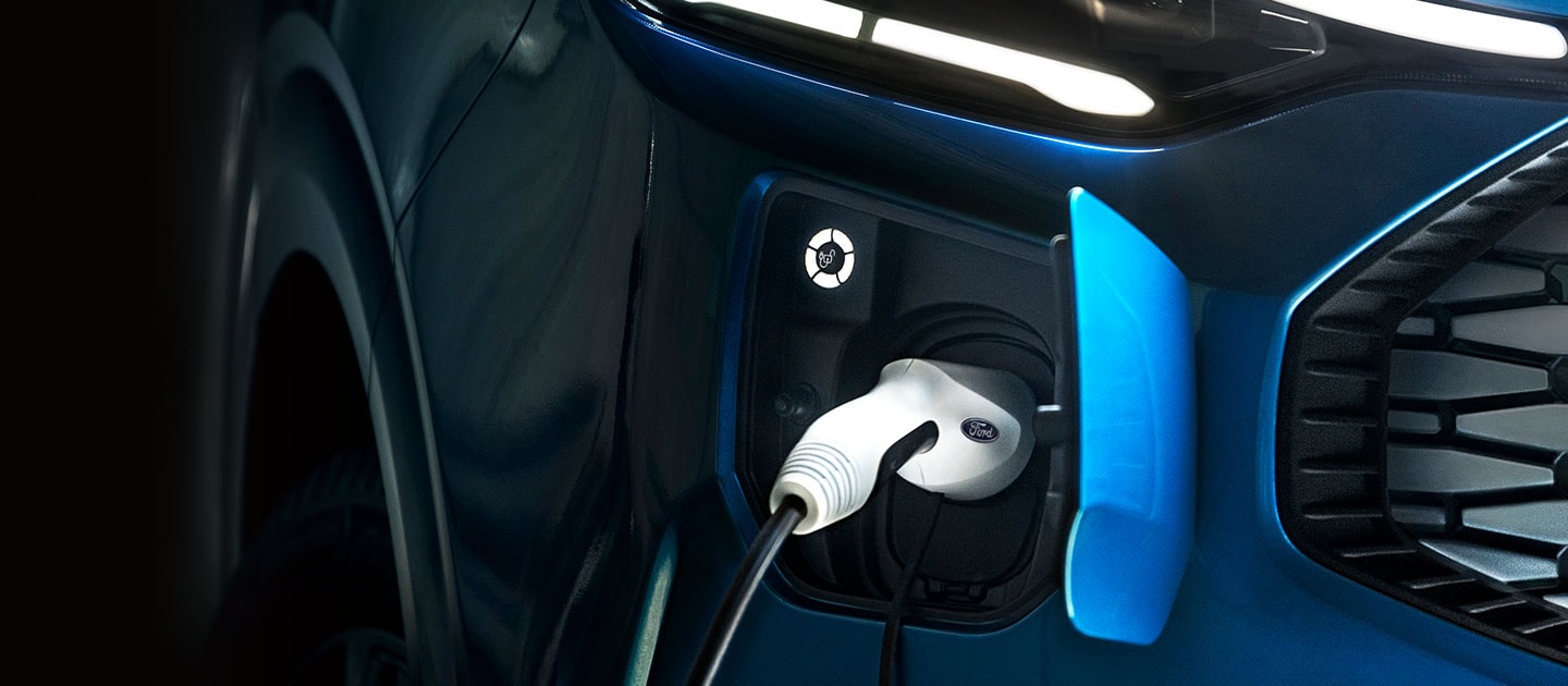 Een close-up van de oplaadpoort van een blauwe Ford Tourneo Custom, met de oplaadkabel aangesloten.