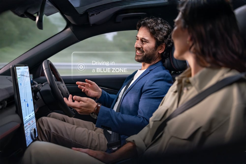 Een man en een vrouw in een Mustang Mach-E rijden handsfree met Ford BlueCruise. Een melding zegt "Rijden in een BLUE ZONE".