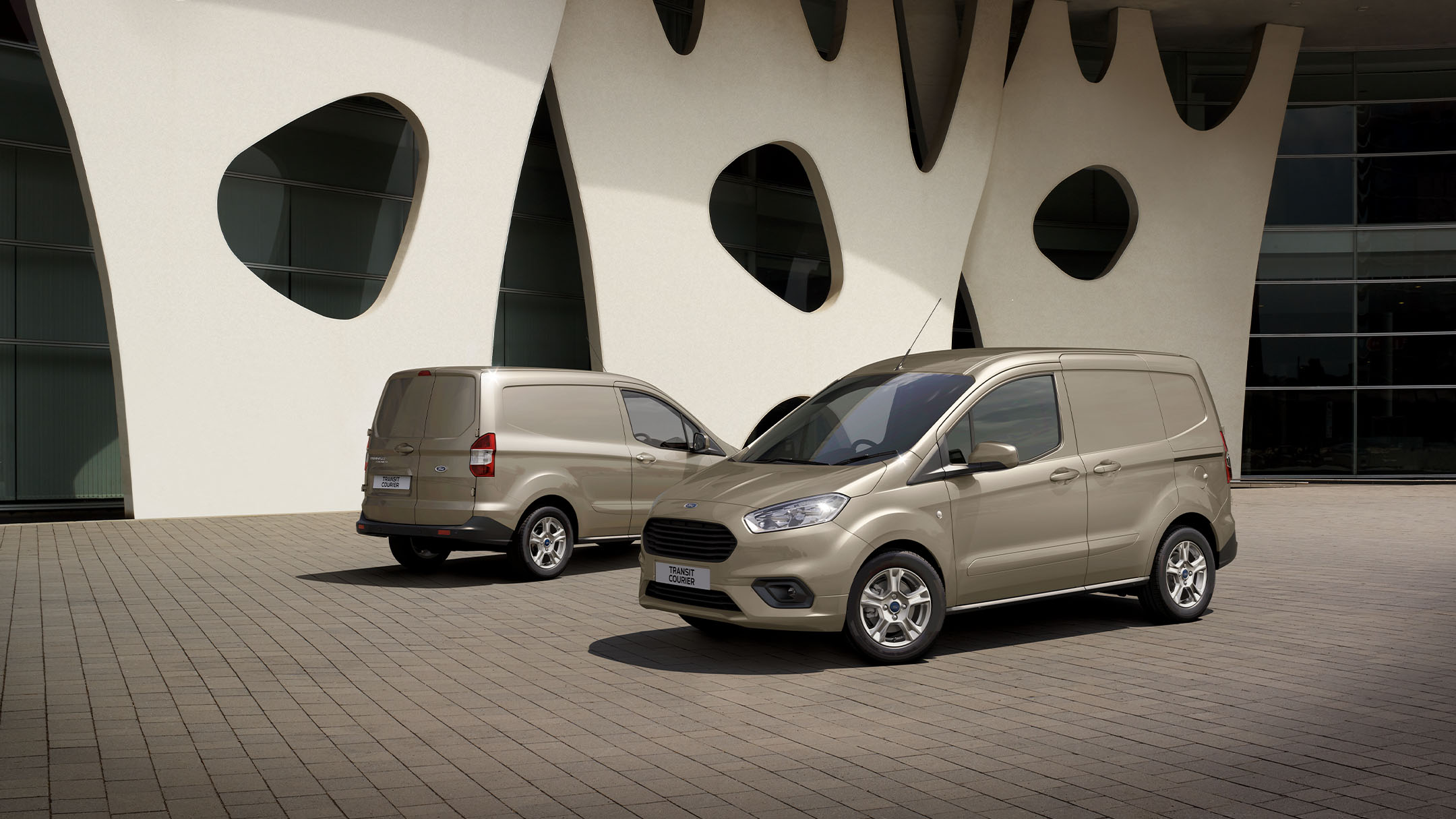 Two Ford Transit Couriers standing side by side next to building