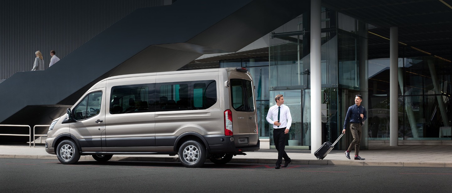 Ford Transit Minibus parked in front of airport with two people and trolly