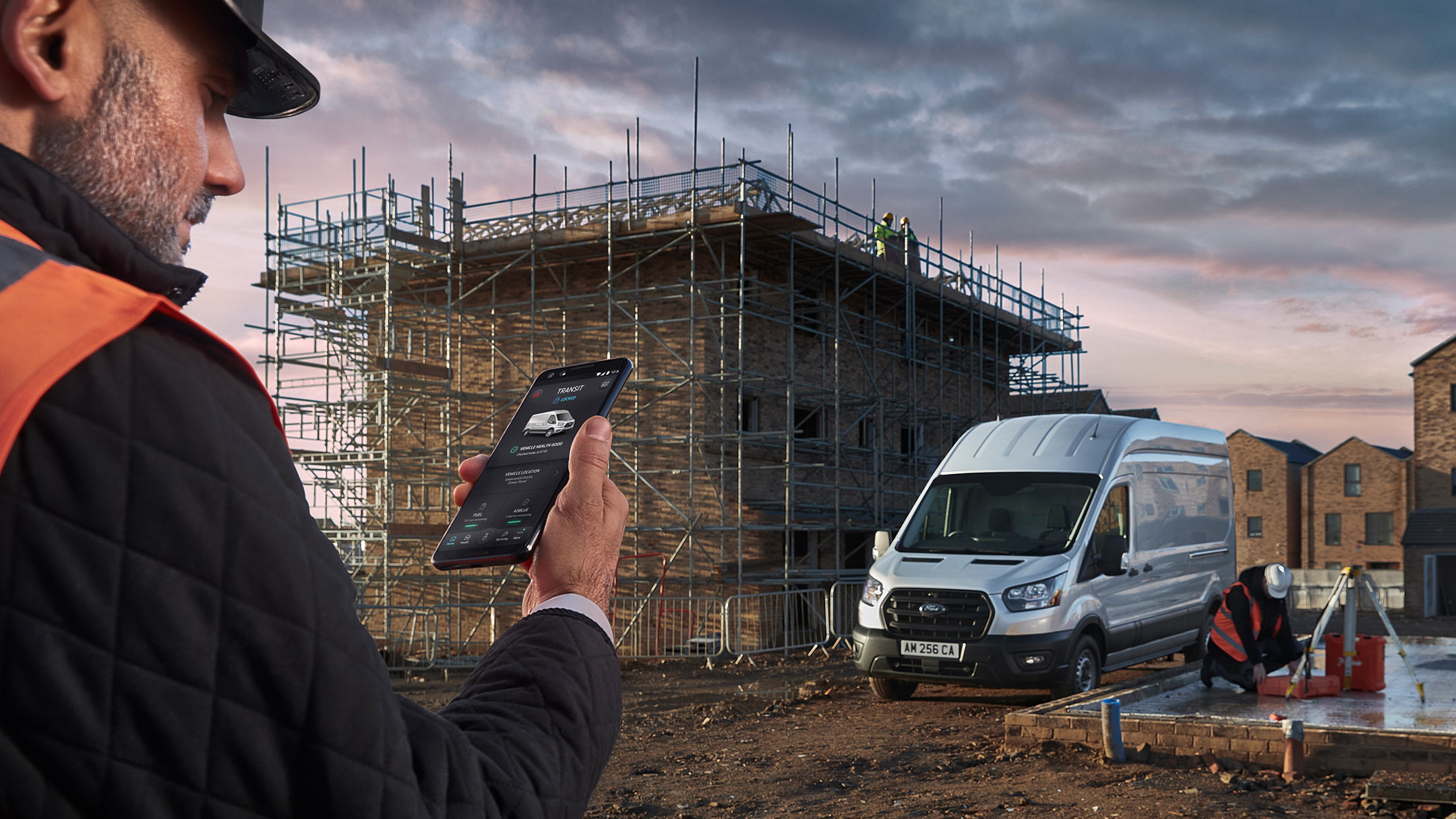 Man kijkt naar zijn mobiele telefoon op een bouwterrein bij een Ford Transit.
