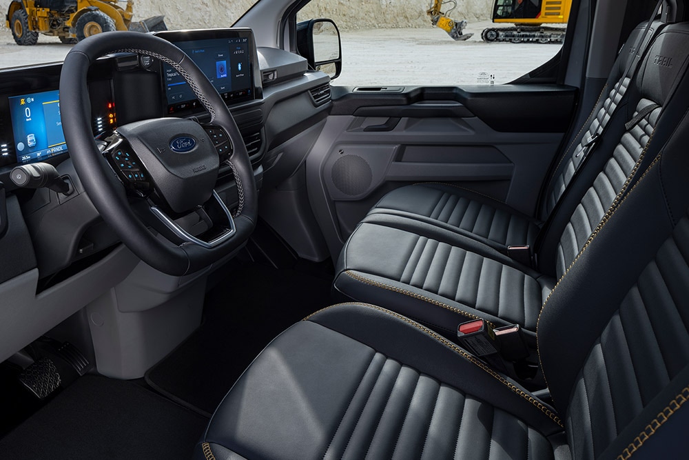 Interieur van een Ford E-Transit Custom Sport elektrische bestelwagen met zwarte en gouden stoelen.