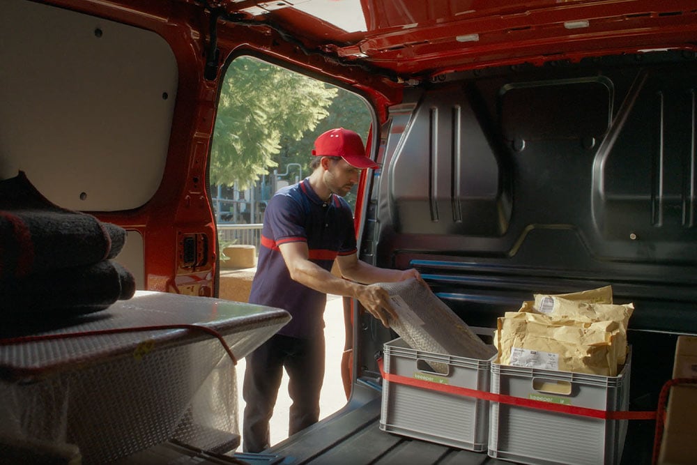 De bezorger lost pakketten van een rode Ford Transit Custom.
