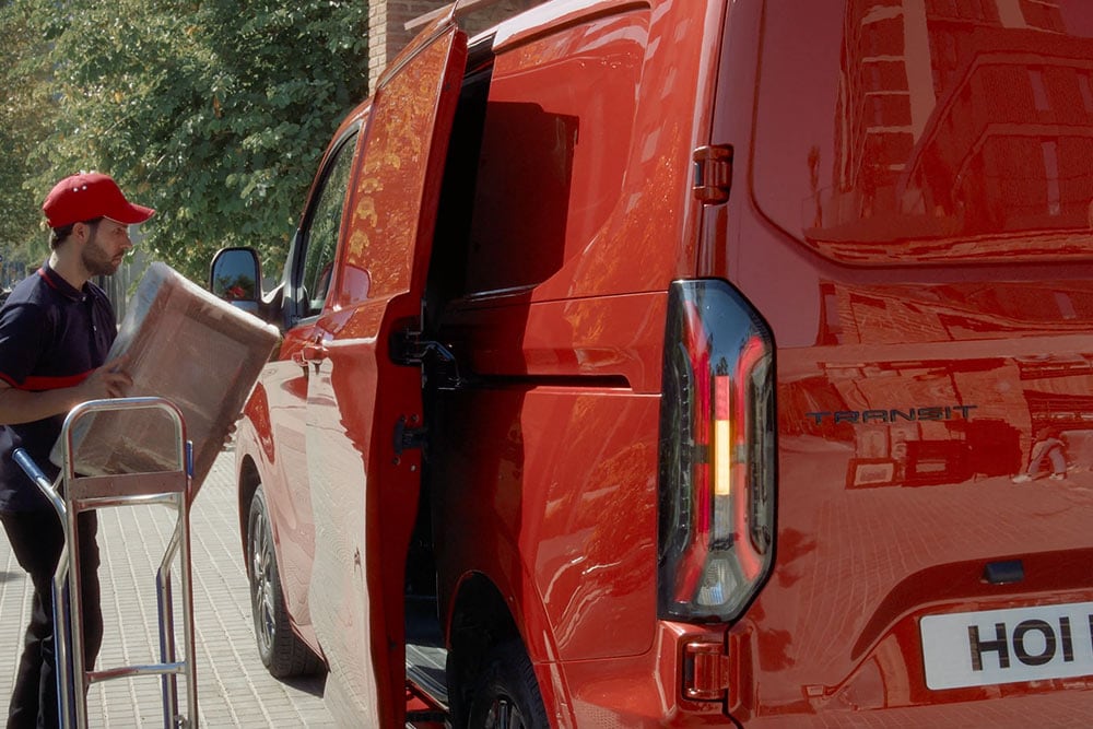De bezorger lost pakketten van een rode Ford Transit Custom.