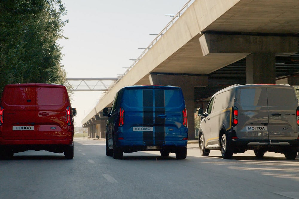 Drie Ford Transit Custom bestelwagens rijden op een snelweg.