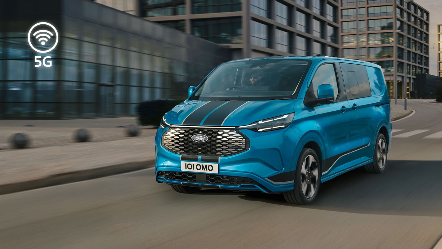 Blauwe Ford E-Transit Custom elektrische bestelwagen rijdt door een stadsstraat.