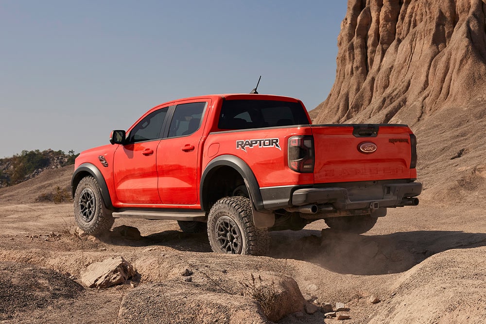 Code Orange Ford Ranger Raptor rijdt offroad bergopwaarts op rotsen.