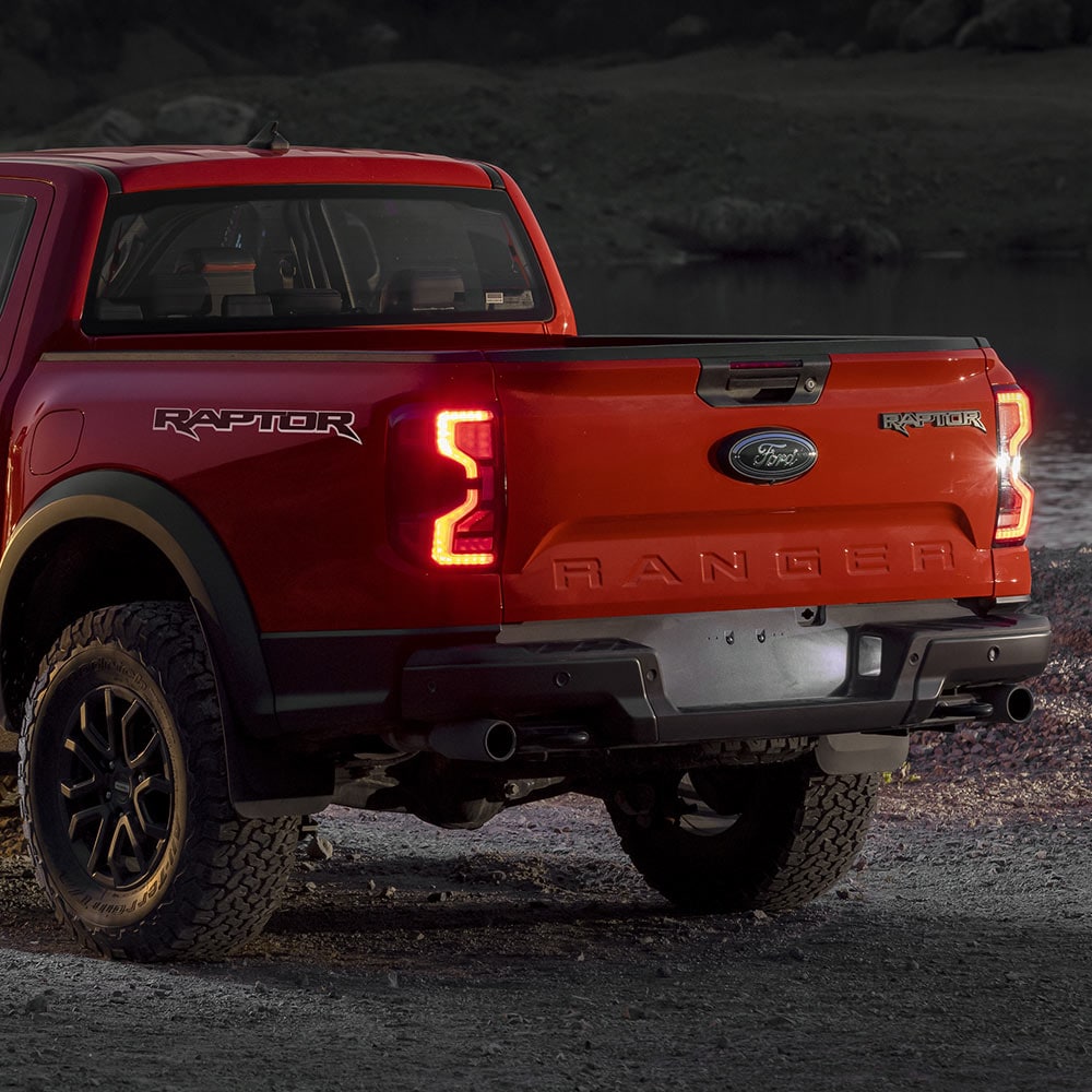 Achteraanzicht van een Ford Ranger Raptor in de kleur Code Orange met achterlichten aan.