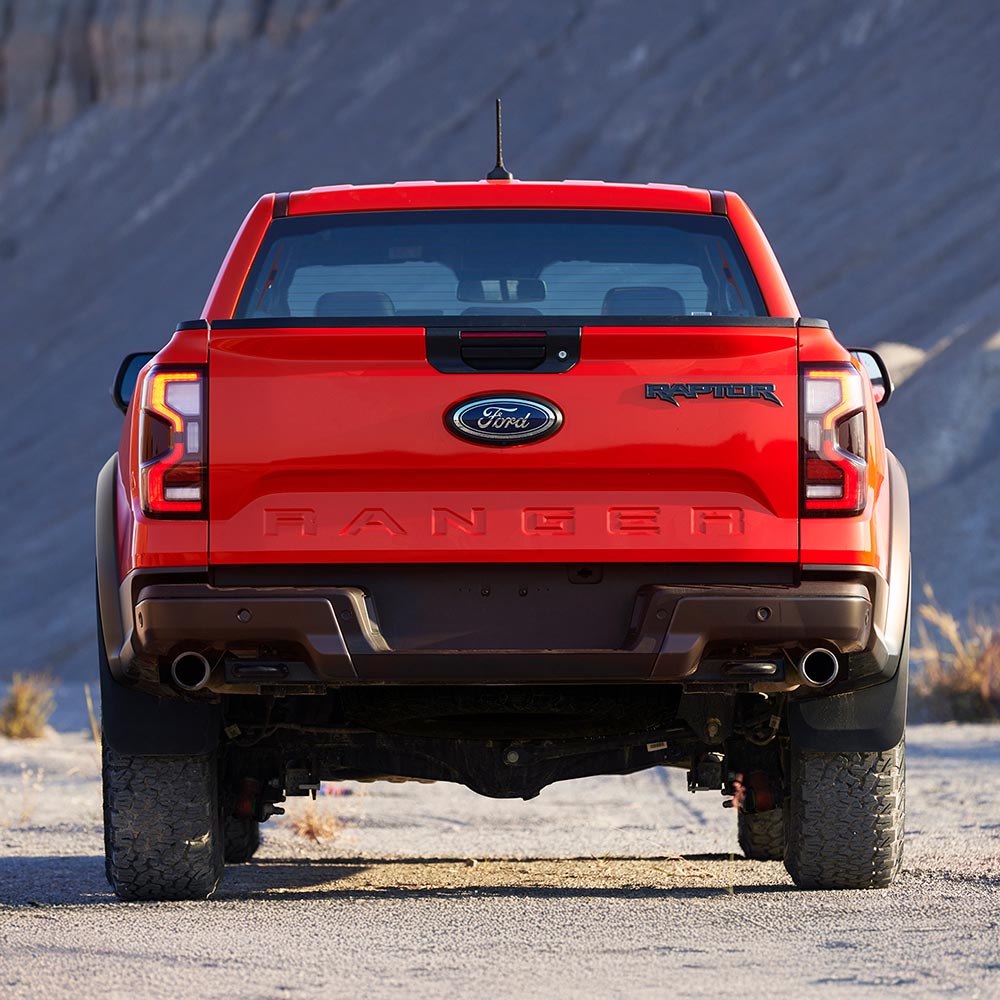 Achteraanzicht van een Ford Ranger Raptor in de kleur Code Orange geparkeerd in de buitenlucht.