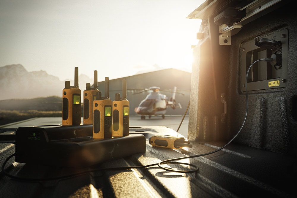 Verschillende walkietalkies worden bij zonsondergang in de laadbak van een Ranger Raptor opgeladen, met in de verte een helikopter.
