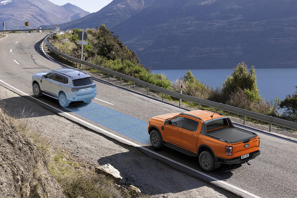 Een gele Ford Ranger Raptor rijdt over een schilderachtige bergroute, met de nadruk op de rijhulpsystemen van het voertuig.