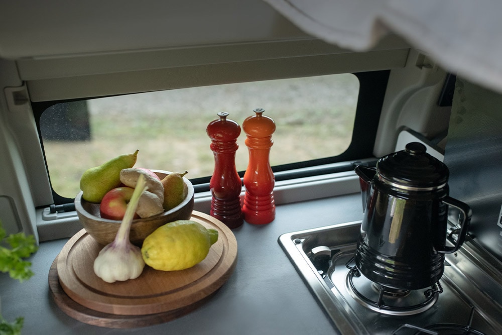 Kookplaat van de Ford Transit Custom Nugget met waterkoker en fruit op het aanrecht.