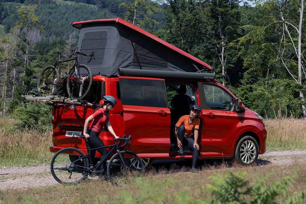 Mensen halen fietsen uit de fietsendrager van een rode Ford Transit Custom Nugget.