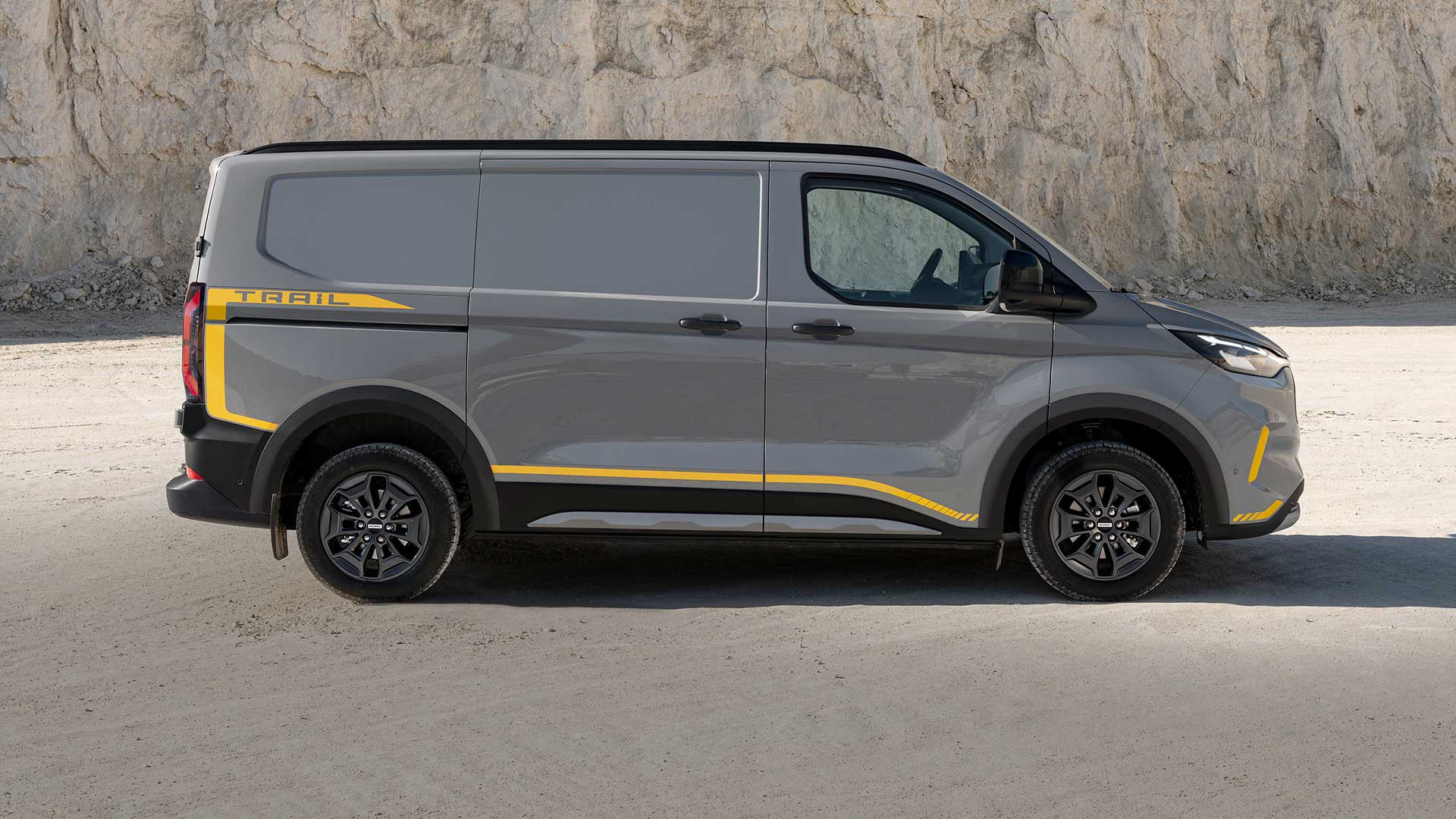 Grijze Ford Transit Custom Trail bestelwagen met gele accenten, zijaanzicht.