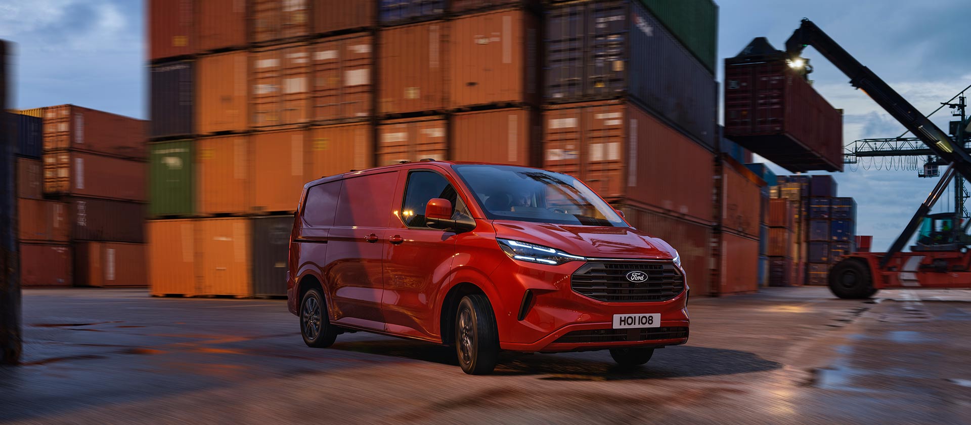 Een rode Ford Transit Custom bestelwagen rijdt door een scheepswerf.