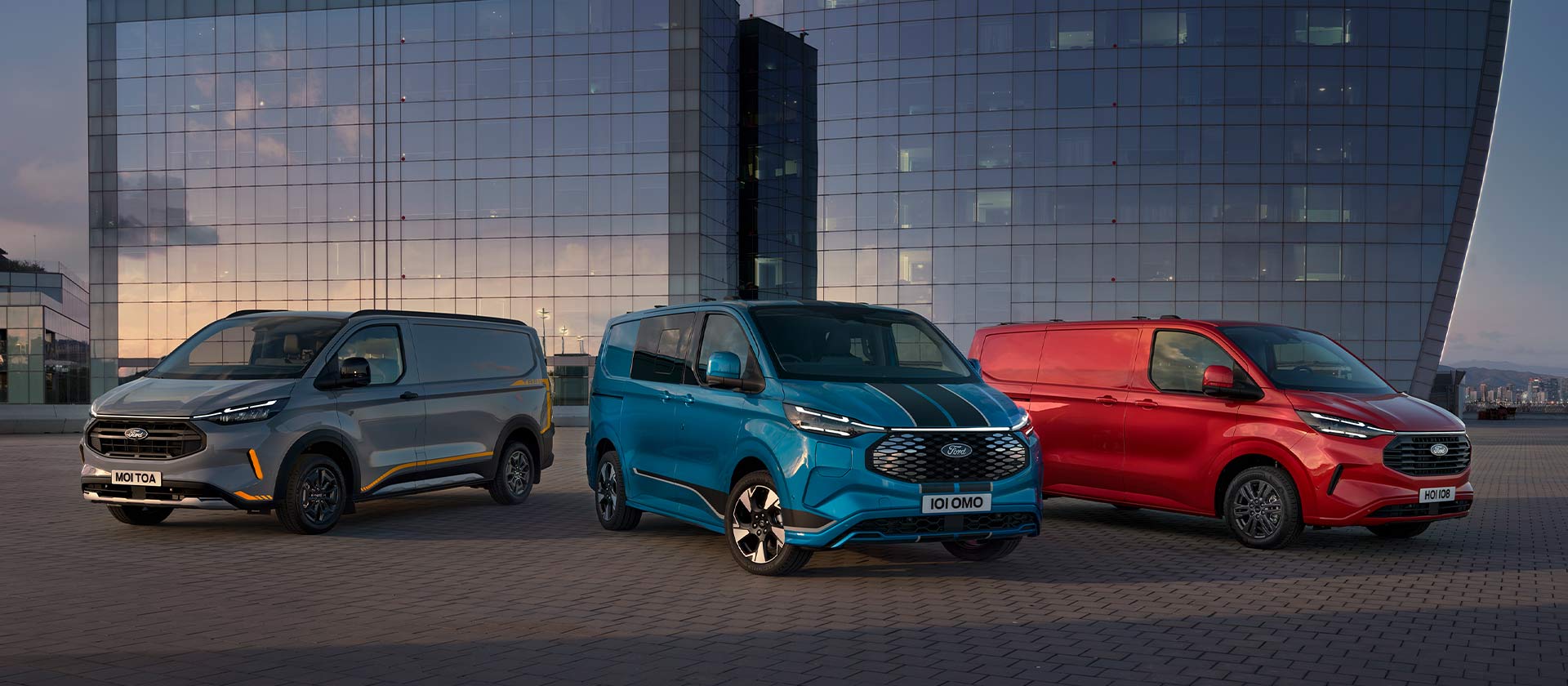 Drie Ford Transit Custom Sport bestelwagens in het grijs, blauw en rood, geparkeerd. 