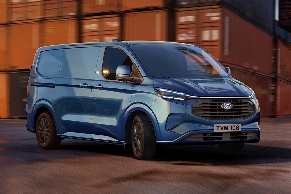 Een blauwe Ford Transit Custom plug-in hybride bestelwagen rijdt door een scheepswerf.