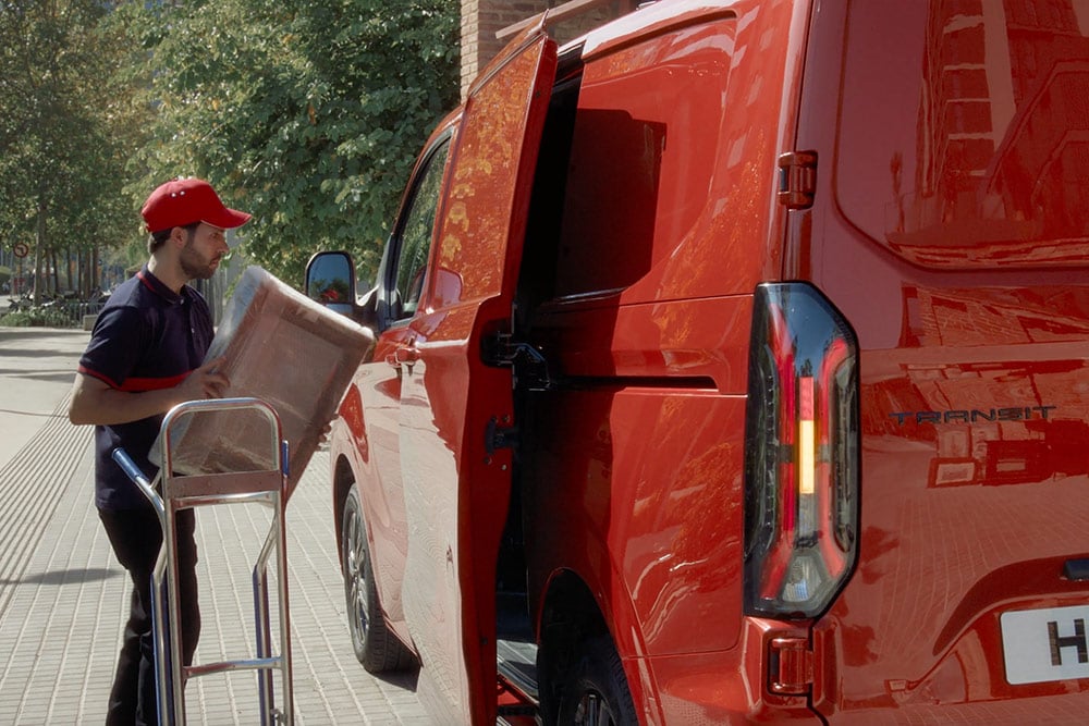 De bezorger lost pakketten van een rode Ford Transit Custom.