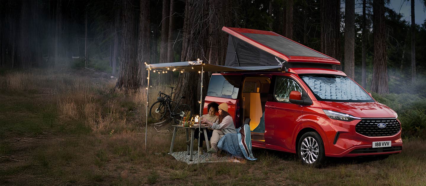Rode Ford Transit Custom Nugget camper, geparkeerd in een bos.