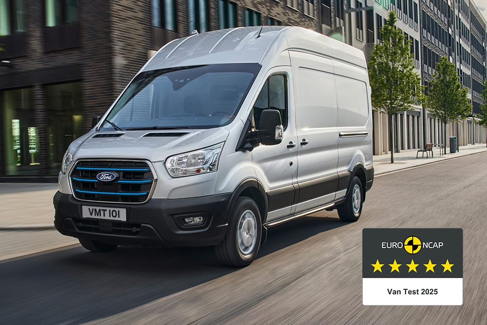Zilverkleurige Ford E-Transit elektrische bestelwagen rijdt op een weg met een 'Gold 2022 Commercial Van Safety'--badge.