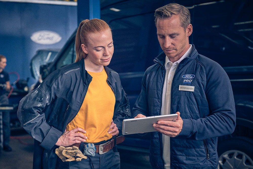 Twee monteurs in een garage kijken naar een tablet voor een Ford E-Transit elektrische bestelwagen.