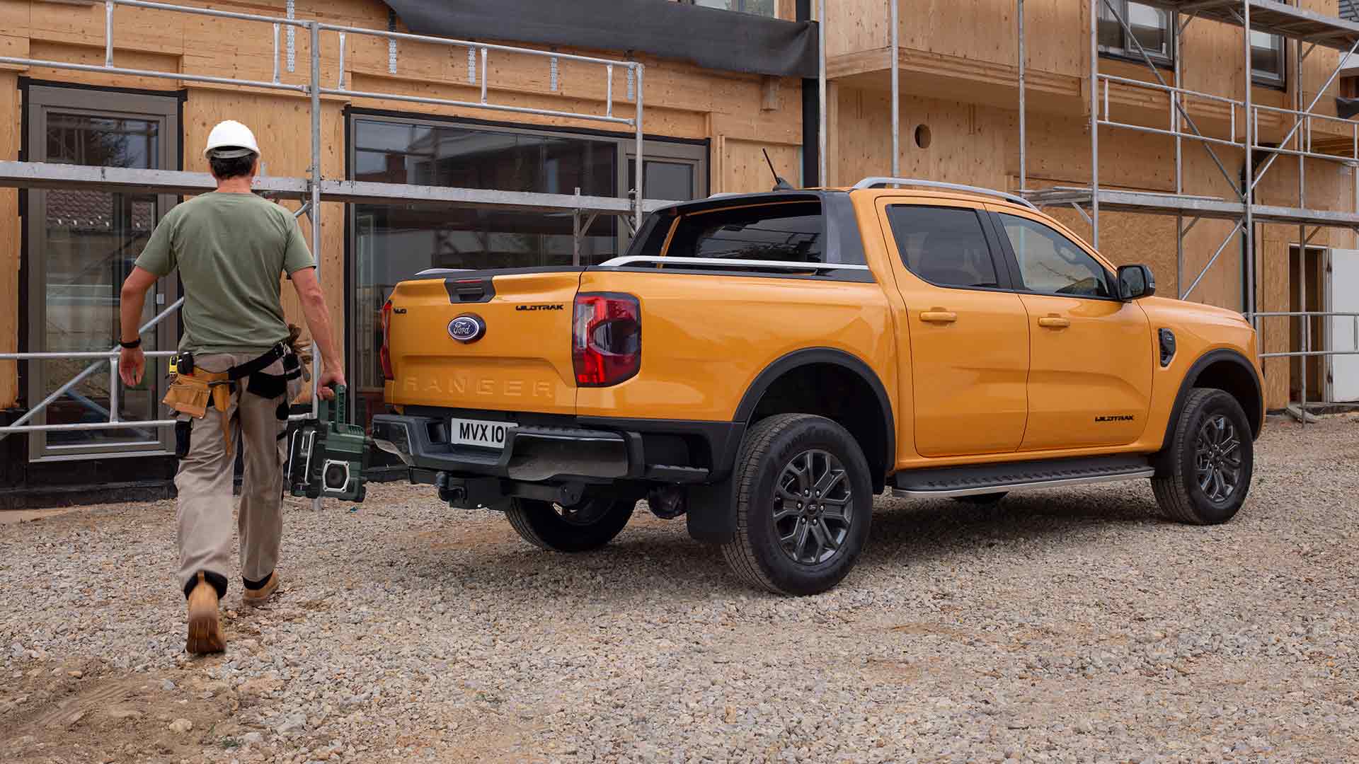 Driekwart achteraanzicht van de gele Ford Ranger Wildtrak Dubbele Cabine op een bouwplaats.