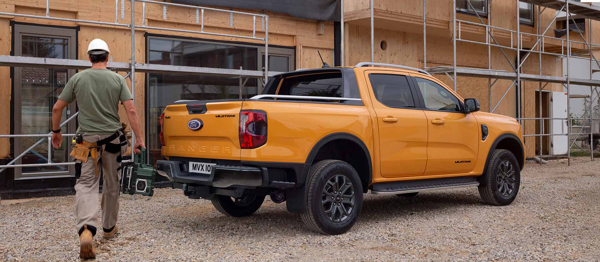 Een arbeider met een helm loopt op een bouwplaats naar een gele Ford Ranger pick-up.