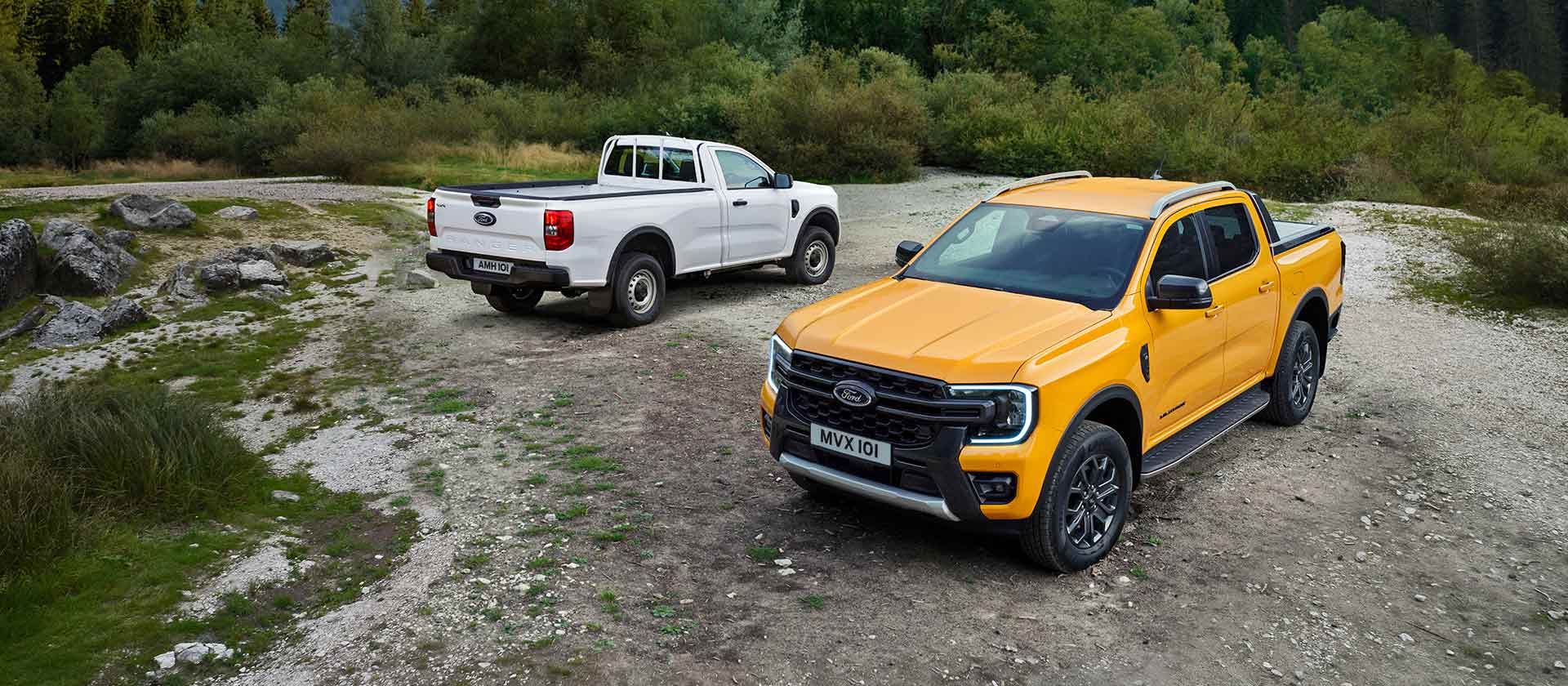 Een witte Ford Ranger en een gele Ford Ranger aan rotsen langs de weg.