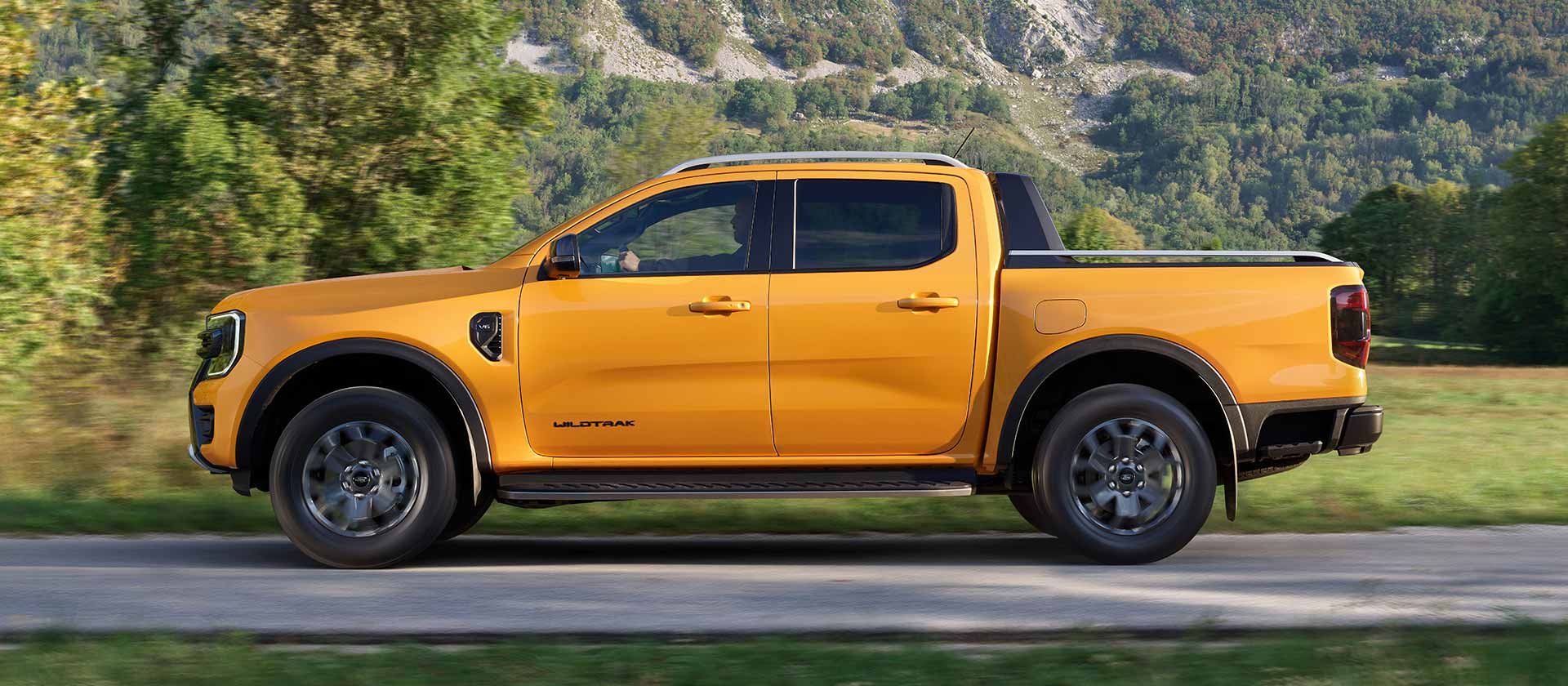 Zijaanzicht van een gele Ford Ranger Wildtrak op een verharde weg.