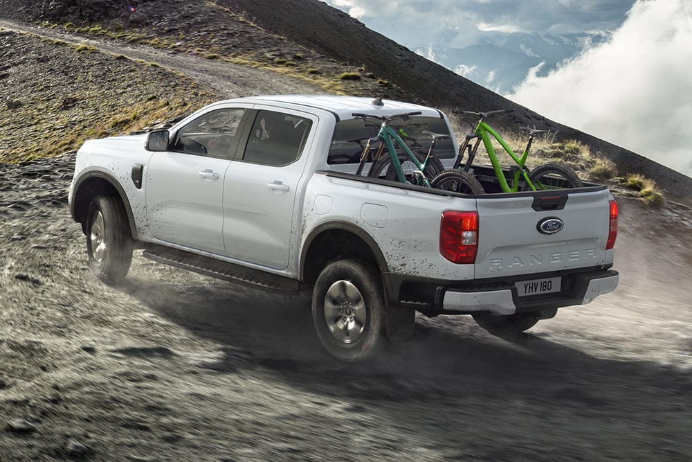Een Ford Ranger Stormtrak PHEV rijdt offroad een heuvel op met twee fietsen in de laadruimte.