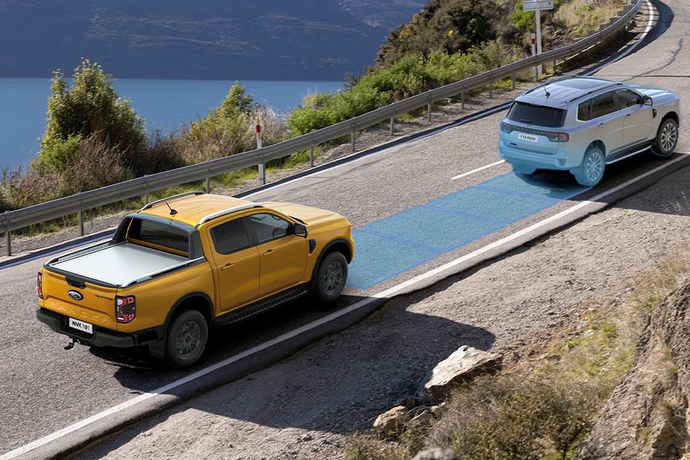 Een gele Ford Ranger gebruikt zijn geavanceerde rijhulpsysteem langs een kustweg. 