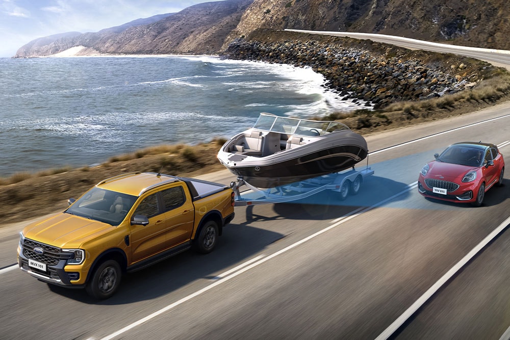 Een gele Ford Ranger sleept een boot langs een kustweg en toont zijn trekvermogen.