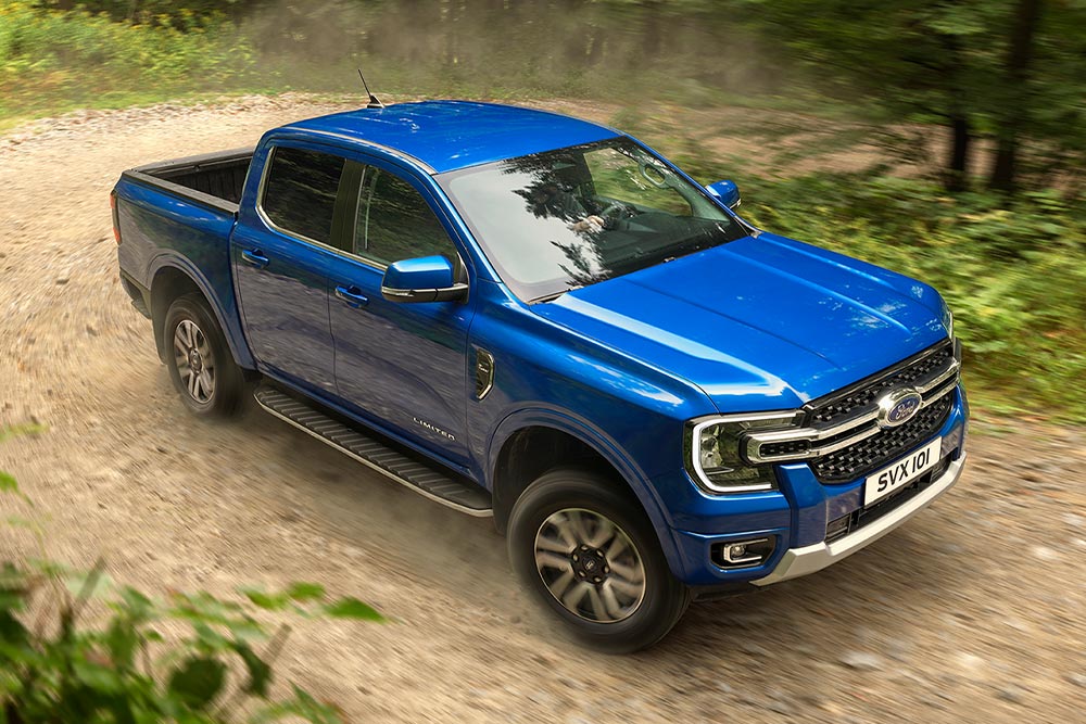 Een blauwe Ford Ranger pick-up rijdt over een onverharde weg door een bos en laat een spoor van stof achter.