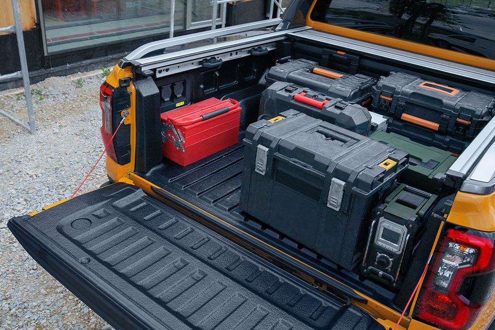 De neergelaten achterklep van een gele Ford Ranger met een houten plank bevestigd met de klem.