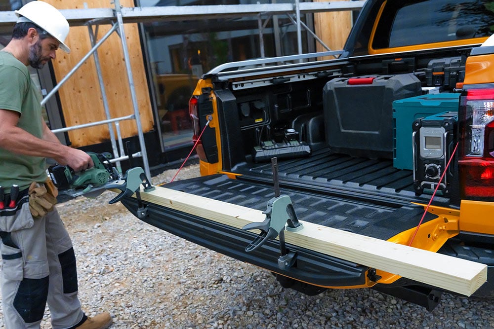 De neergelaten achterklep van een gele Ford Ranger met een houten plank bevestigd met de klem.