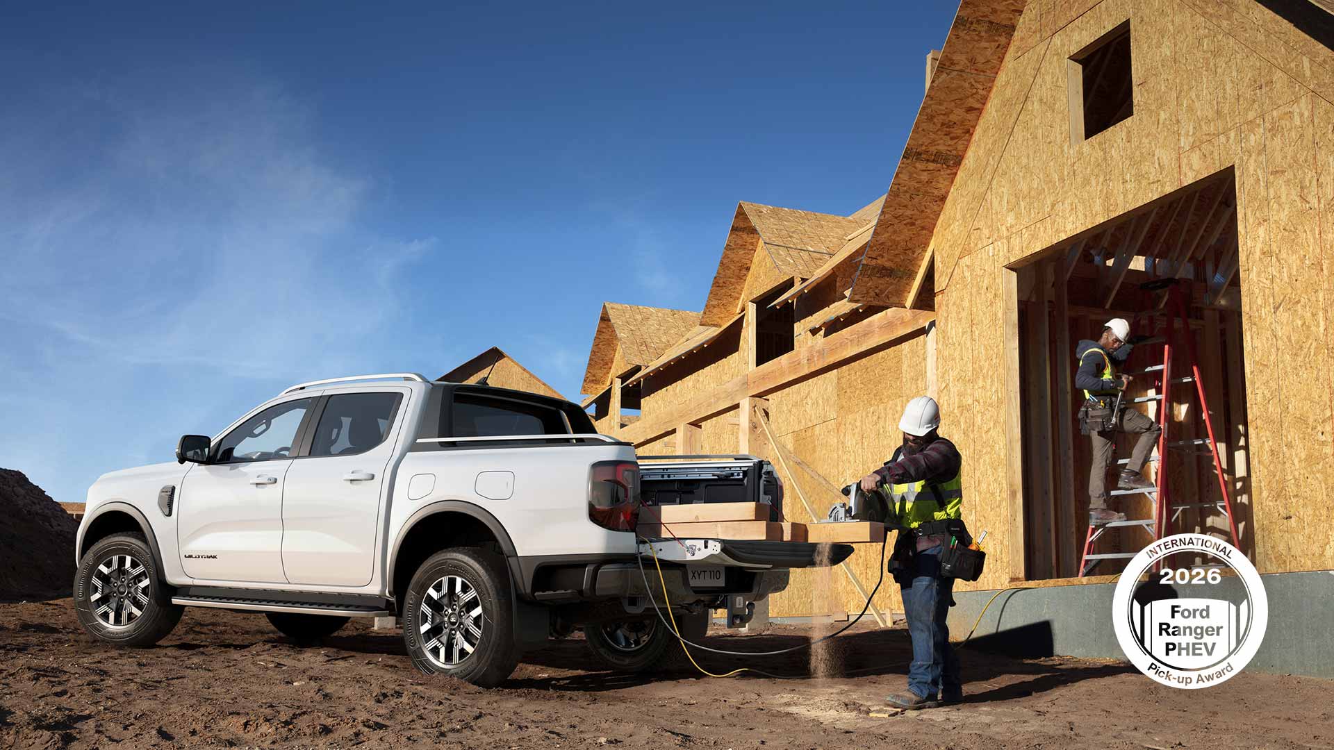 Witte Ford pick-up geparkeerd op een bouwterrein, met de motor van een zaagmachine aan het werk terwijl een bouwvakker hout zaagt.