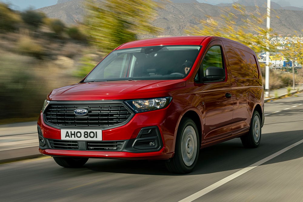 Een Ford Transit Connect rijdt op een weg, met zichtbare grille en automatische koplampen.