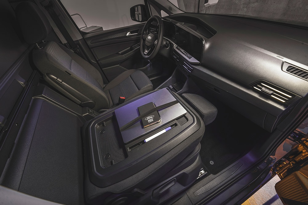Interieur van een Ford Transit Connect met dashboard, stoelen, een laptop en telefoon op de middenconsole.