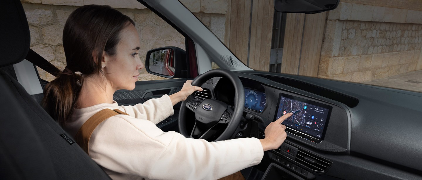Een vrouw raakt het 10" touchscreen aan terwijl ze op de bestuurderszetel van de nieuwe Ford Transit Connect zit.