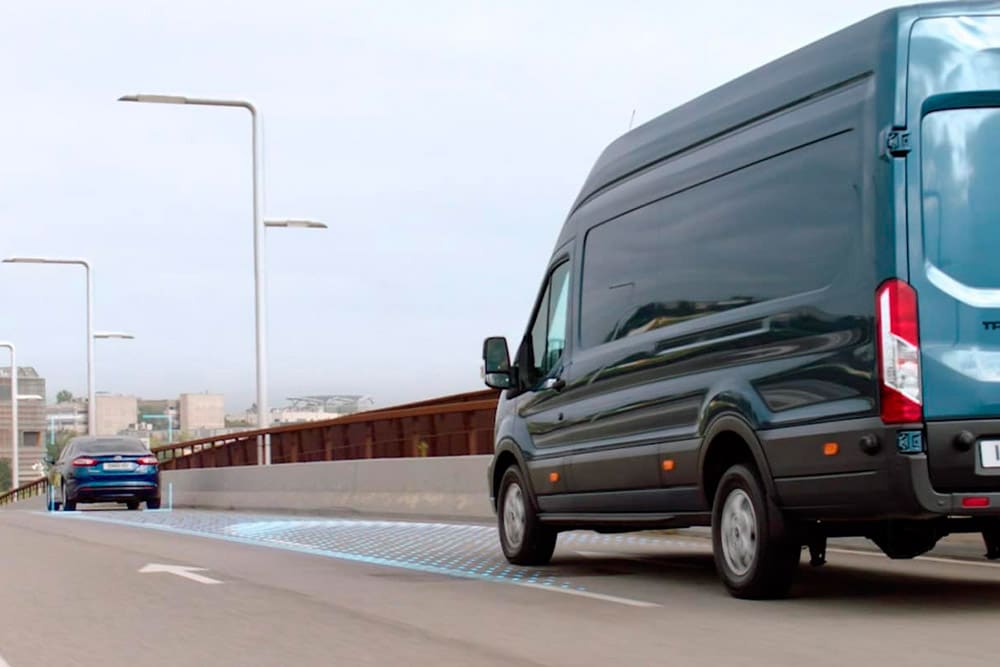 Blauwe Ford Transit bestelwagen met blauwe lijnen op de weg die het gebruik van geavanceerde rijhulpsystemen weergeven.
