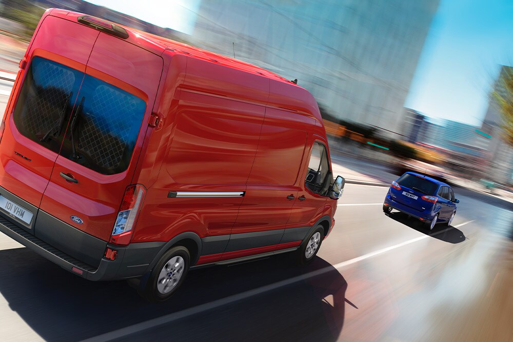 Rode Ford Transit bestelwagen rijdt op een weg.