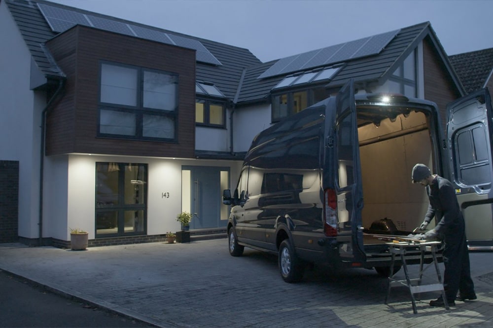 Een timmerman werkt in het donker achter een Ford Transit bestelwagen met open achterdeuren, verlicht door de led-downlighter.
